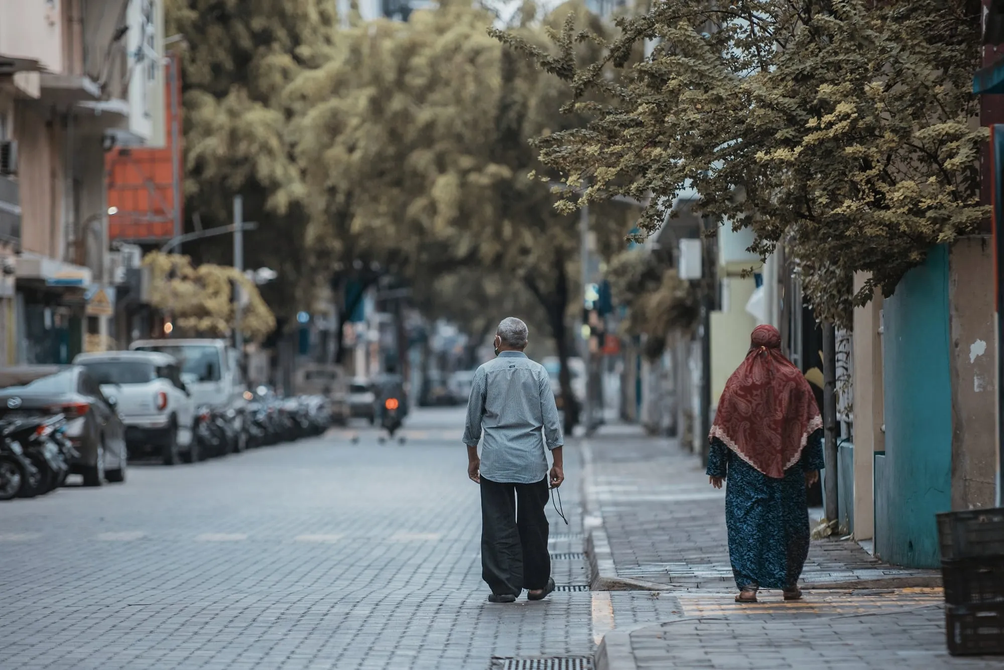 A quiet tree-lined street in Malé in the morning, with parked motorbikes